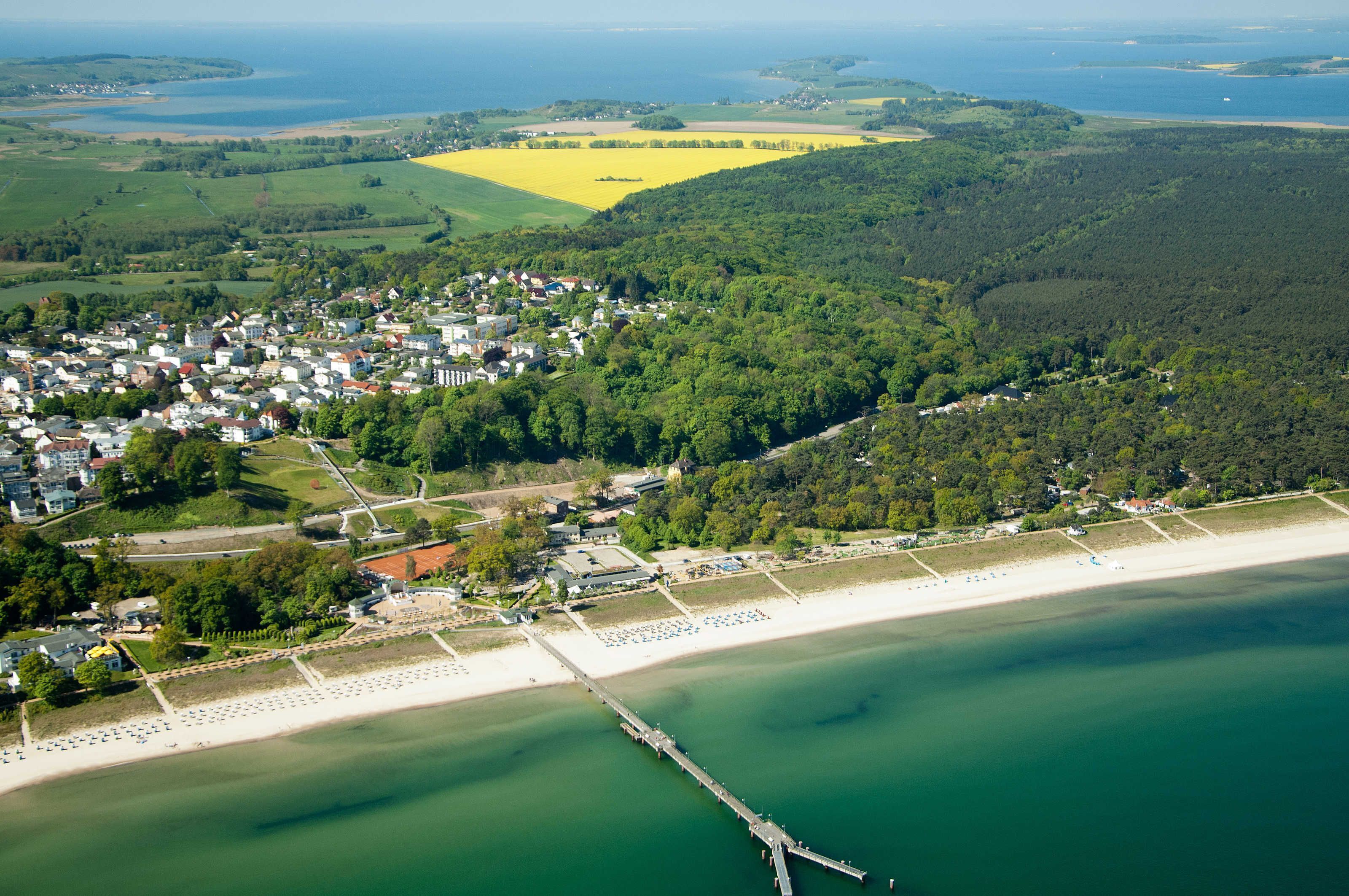 Luftaufnahme einer Küstenstadt mit Strand, Steg und umliegender Vegetation.