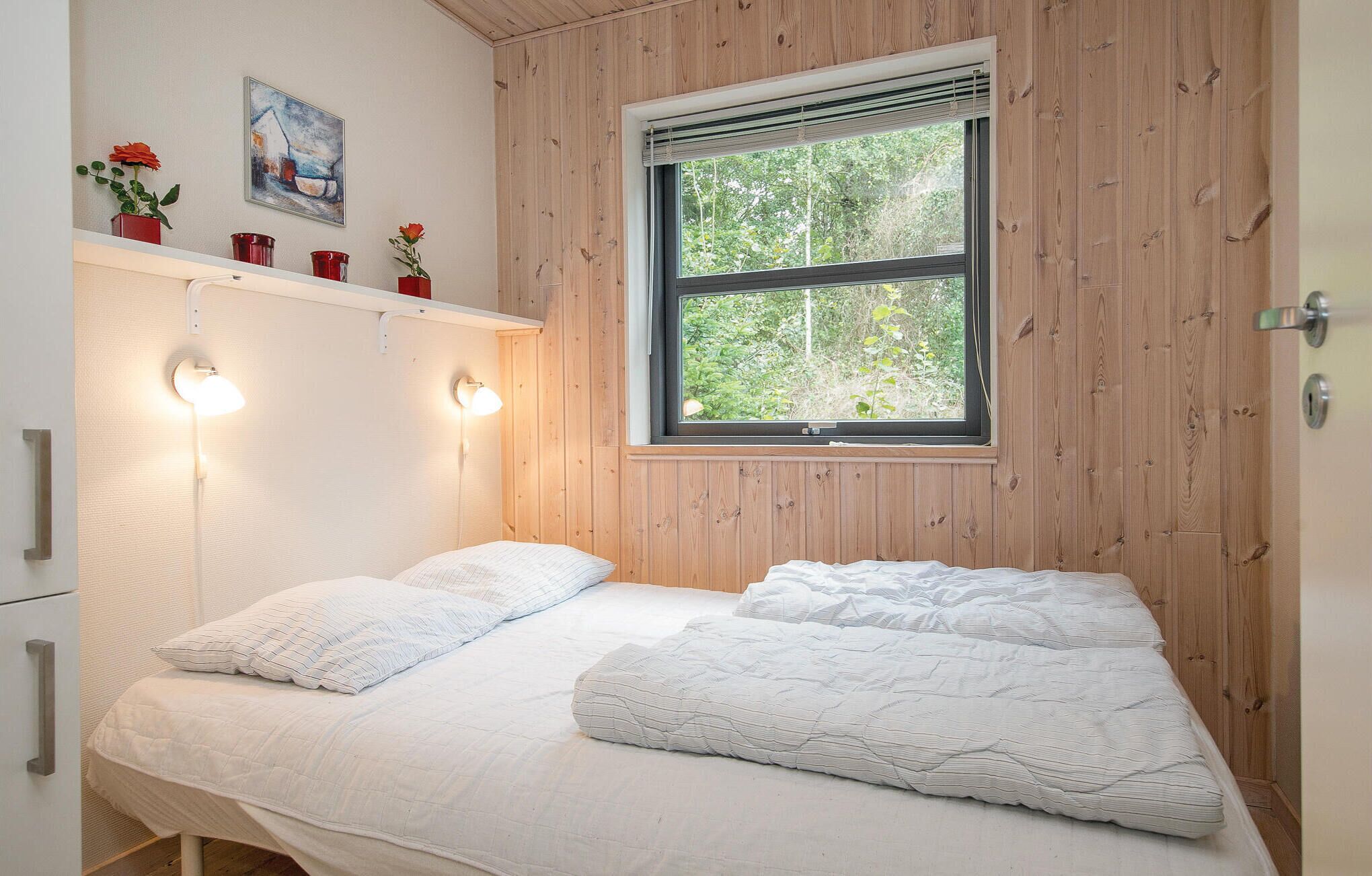 A bedroom with a bed, two bedside lamps, a window with a view of trees, and a painting on the wall.