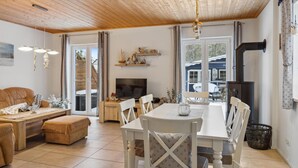 A cozy living room with a wooden ceiling, a TV, a dining table with chairs, and a fireplace. - Ferienhaus 44 Altefähr (Altefähr/Rügen)