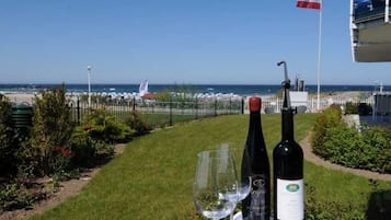 A table with two wine bottles and a glass, a flag, and a view of the sea and beach.