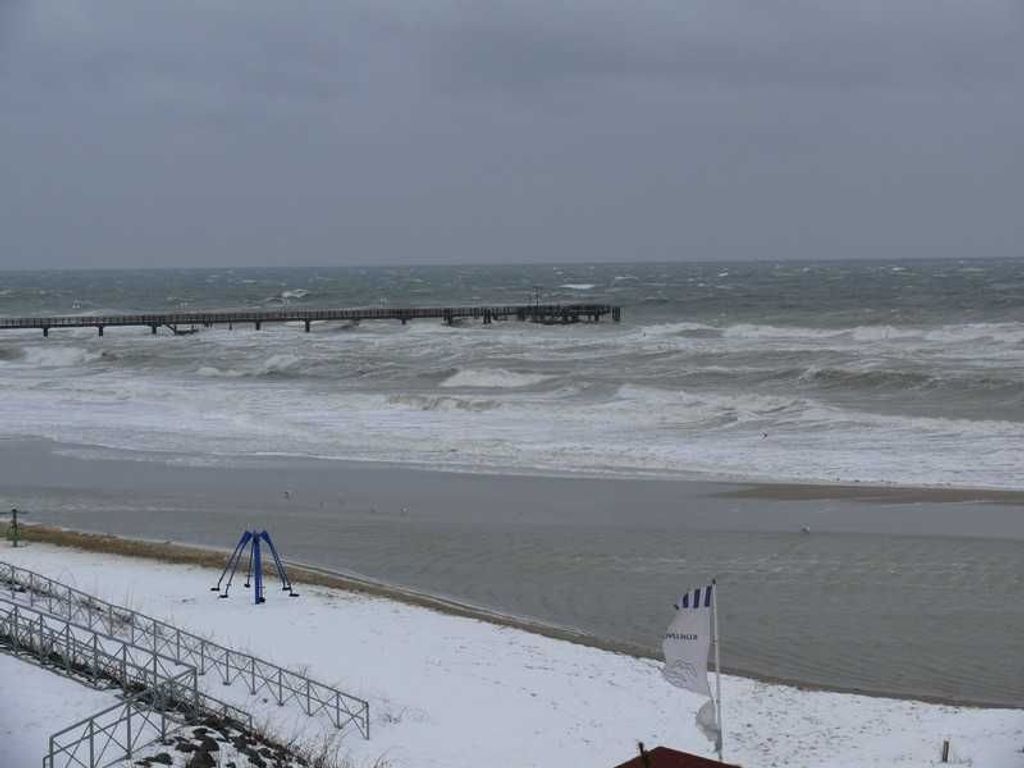 Ein verschneiter Strand mit einem Pier, der sich ins Wasser erstreckt.