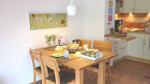 Un comedor con una mesa de madera, sillas, un cuadro en la pared y una cocina al fondo.