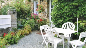 Une terrasse de jardin avec des chaises et une table en plastique blanc, entourée de différentes plantes et fleurs.