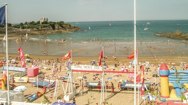 Une plage bondée, avec des structures gonflables et une tour de surveillance des sauveteurs.