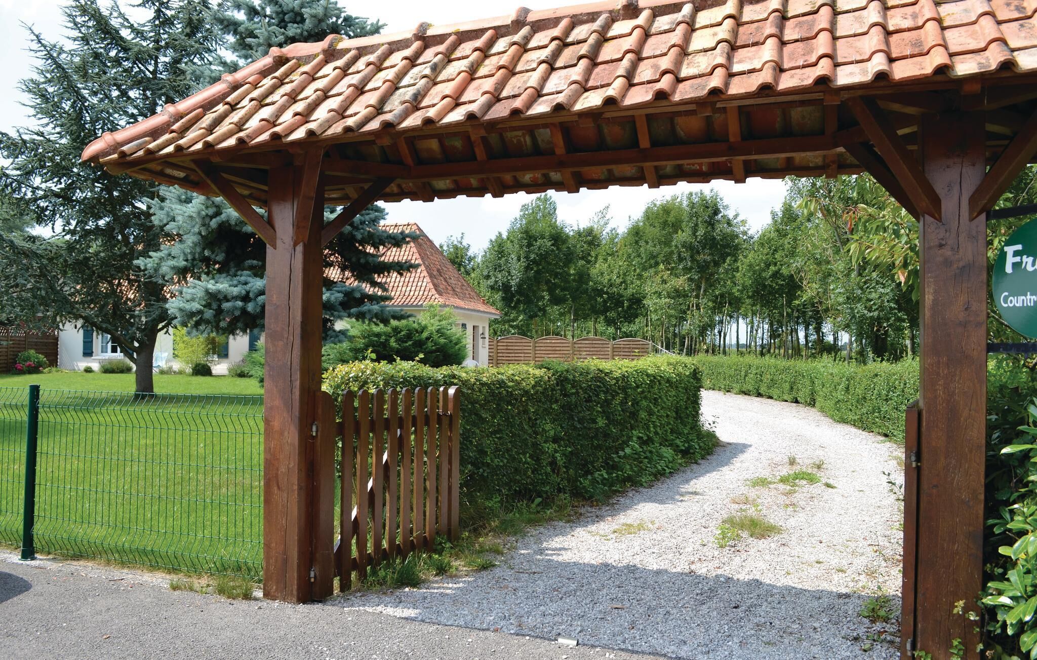 A wooden pergola with a tiled roof, a gravel path, and a green hedge.