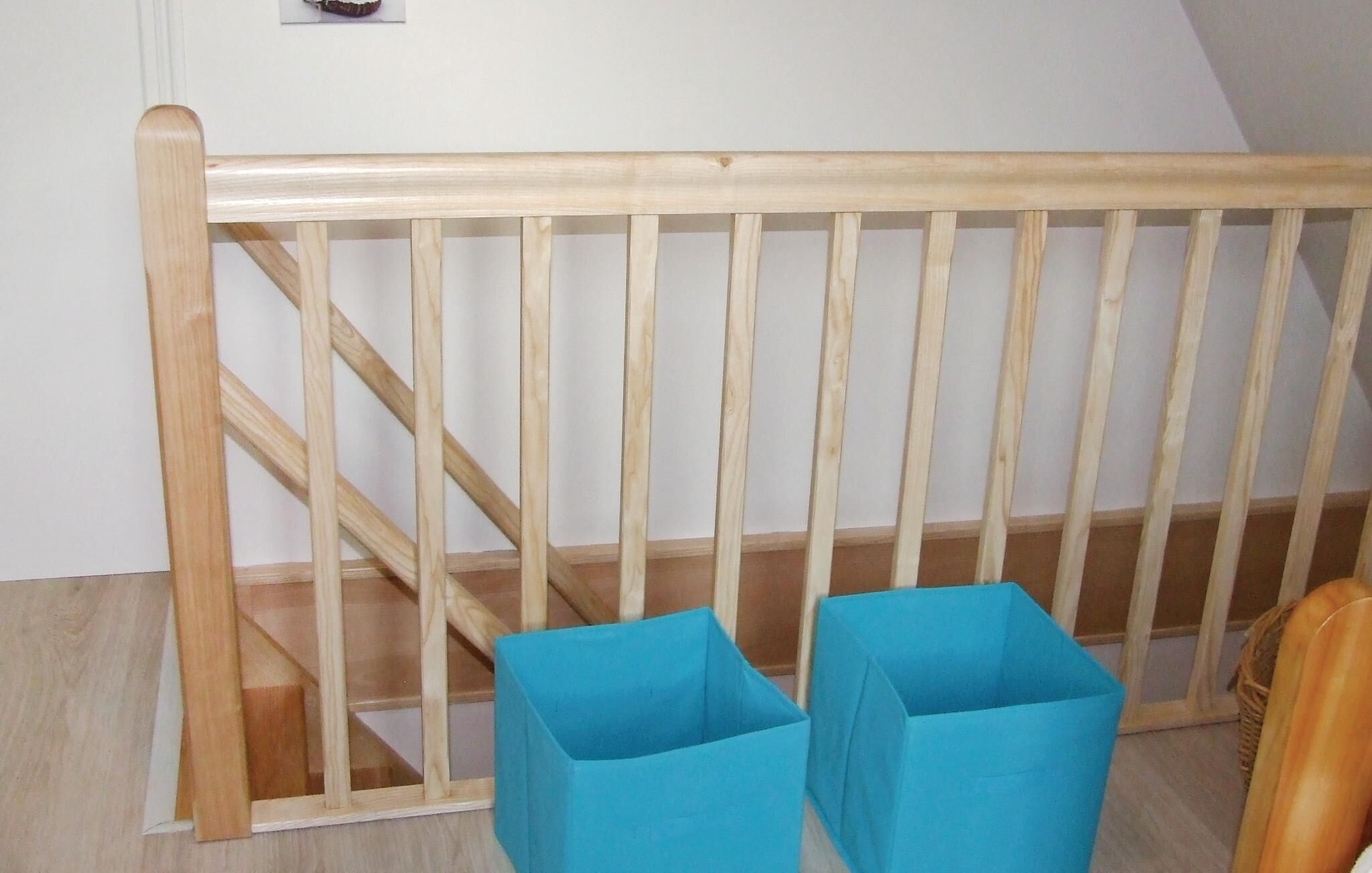 A wooden staircase with a handrail and two blue storage bins at the bottom.