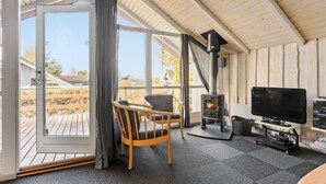 Ein gemütlicher Raum mit Holzvertäfelung, einem Kamin, einem Fernseher und Blick ins Freie.