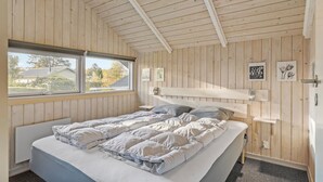 Ein Schlafzimmer mit Holzbalkendecke, einem großen Fenster, einem Bett mit weißer Bettwäsche und einem Kopfteil.