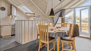 Ein Essbereich mit Holztisch und -stühlen, eine Küche mit Herd und Backofen sowie ein großes Fenster mit Ausblick nach draußen.