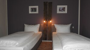 Una habitación con dos camas, suelo de madera y dos lámparas fijadas a la pared.