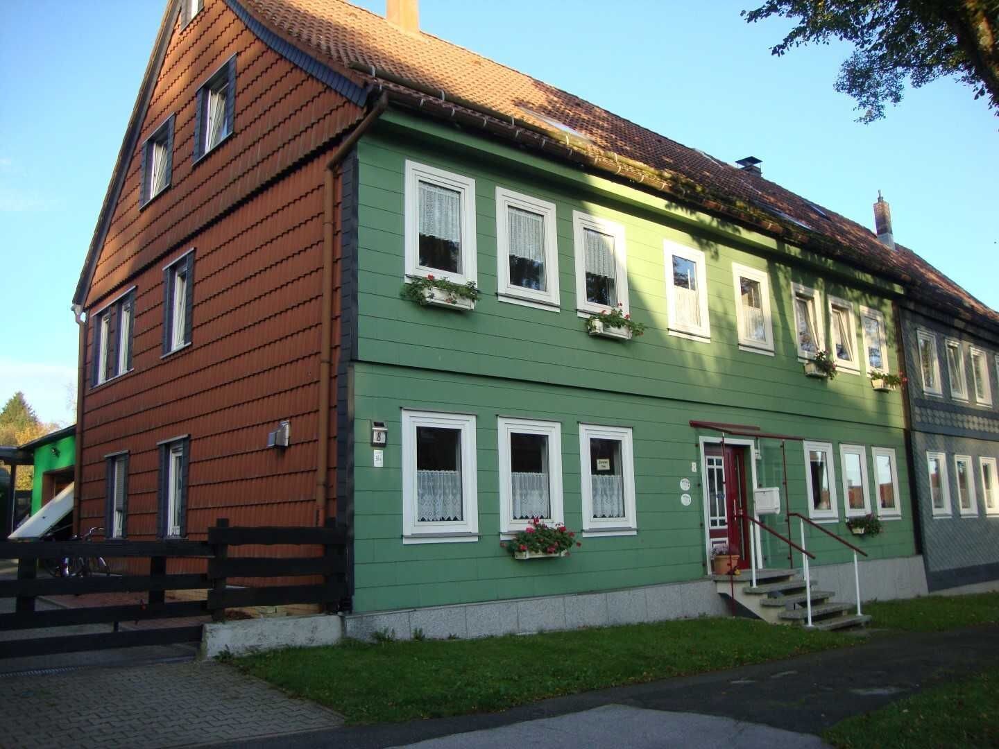 Un edificio de dos pisos con fachada verde, marcos de ventana blancos y puerta roja.