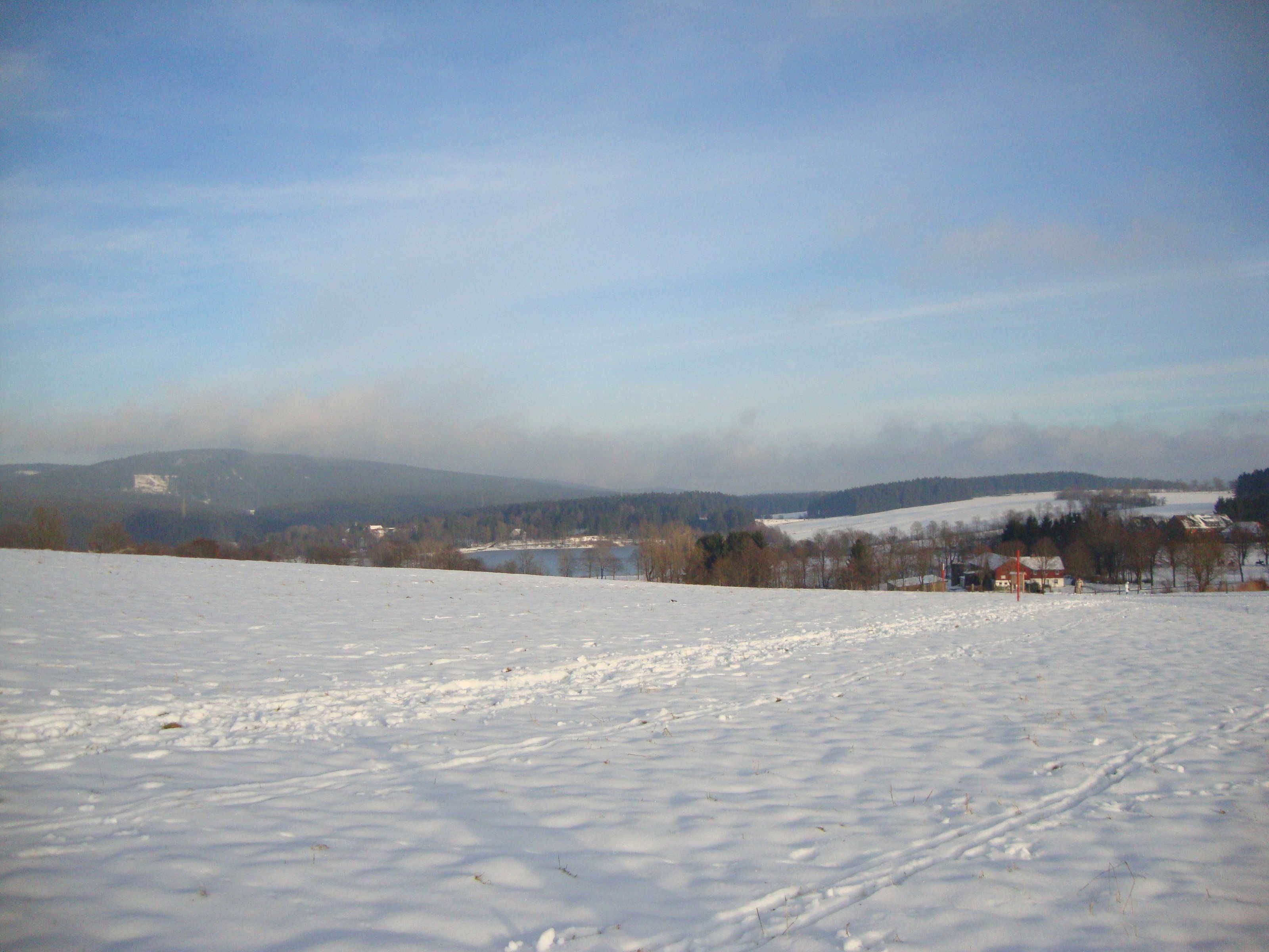 A snowy landscape with a clear sky, distant hills, and a few buildings.