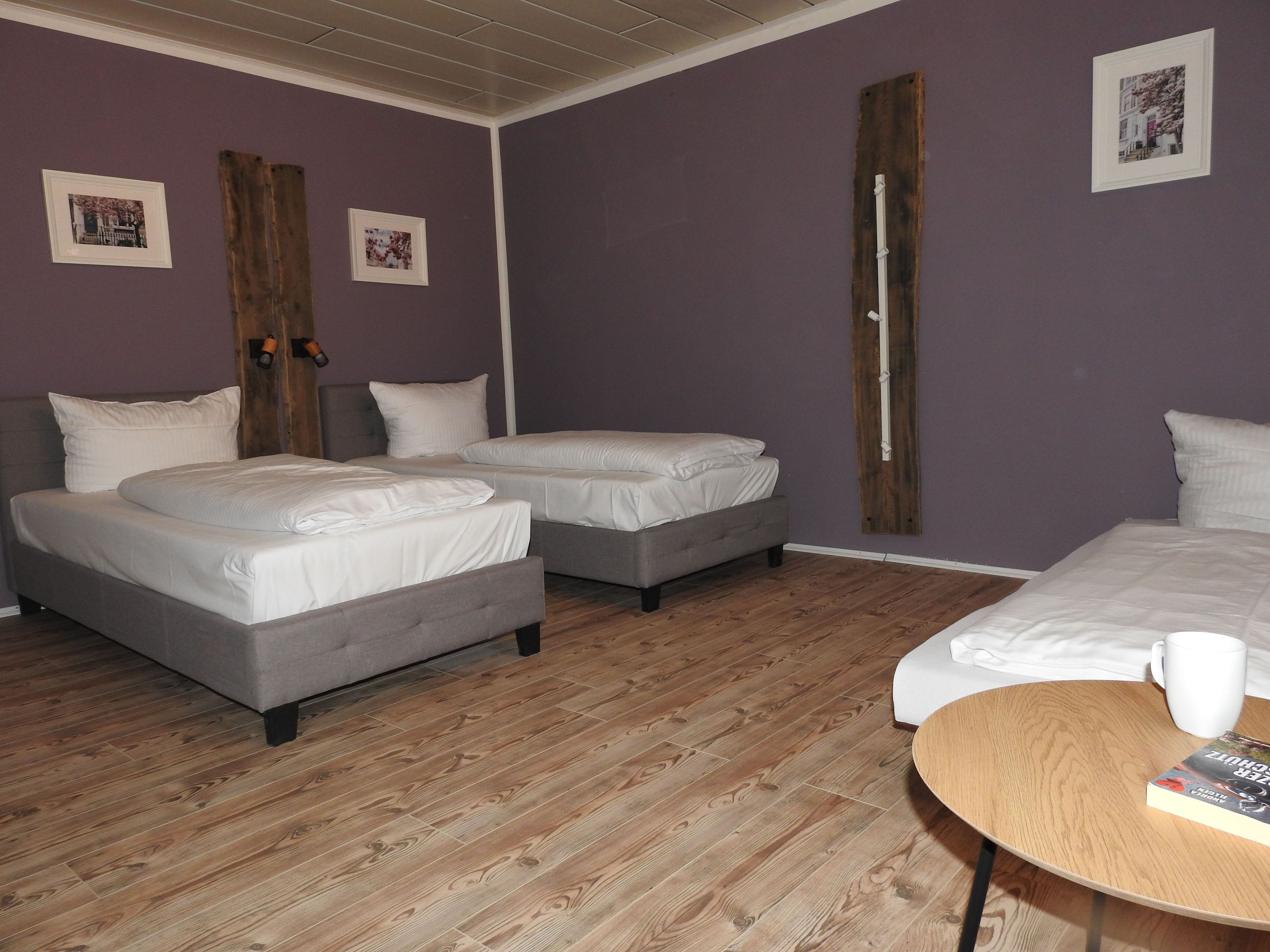 Une chambre avec deux lits, un plancher en bois et une table sur laquelle se trouvent un livre et une tasse.