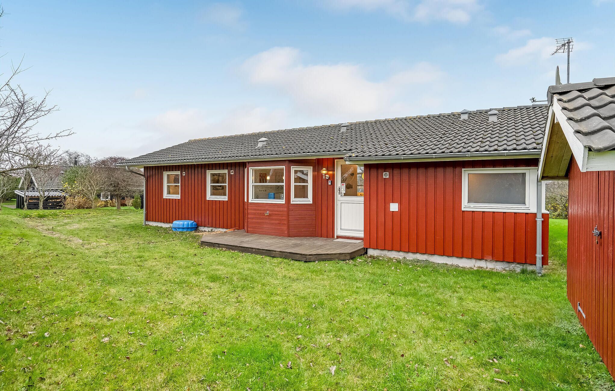 A red single-story house with a tiled roof, a front porch, and a small garden area.