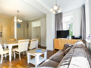 A living room with a sofa, a dining table with chairs, a TV, and a bookshelf.