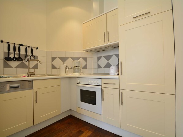 A compact kitchen with white cabinets, a built-in oven, a coffee maker, and a sink.