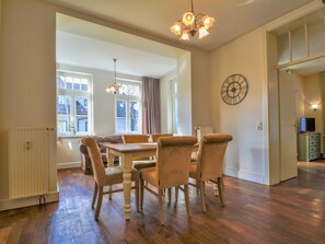 Ein geräumiger Essbereich mit Holztisch und Stühlen, einer Kristallleuchtre und großen Fenstern mit Vorhängen.