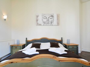 Ein ordentlich bezogenes Bett mit einem Holzkopfteil, zwei Nachttische mit Lautsprechern und ein an der Wand hängendes Kunstwerk darüber.