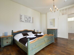 Een slaapkamer met een houten bed, nachtkastjes, een dressoir en kunstwerken aan de muur.