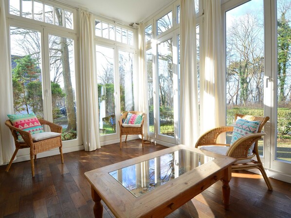 A sunlit room with large windows, wicker chairs, and a glass-top table.