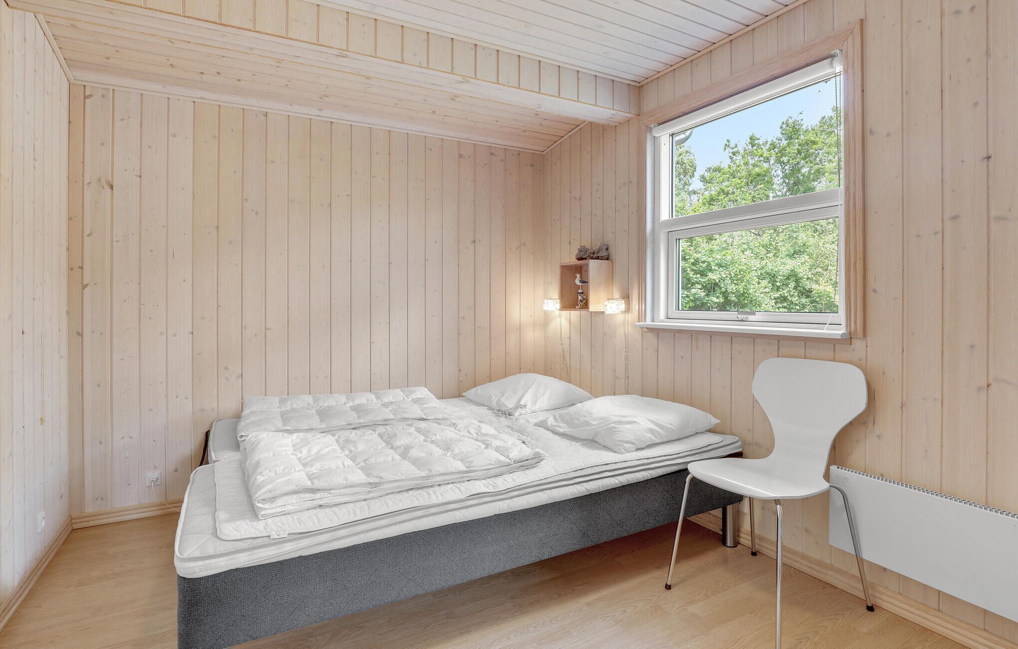 Ett sovrum med en säng, en stol, ett fönster och en hylla som är monterad på väggen.