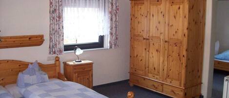 Una camera da letto con un letto di legno, un comodino con una lampada, un armadio in legno e una finestra con tende floreali.
