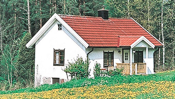 Une maison blanche avec un toit rouge, une véranda en bois et un petit jardin parsemé de fleurs jaunes.