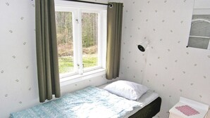 Une petite chambre avec un lit simple, une fenêtre, une table de chevet et une lampe fixée au mur.