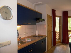 Una cocina con un reloj, armarios de madera, un lavabo y una ventana con cortinas rojas.
