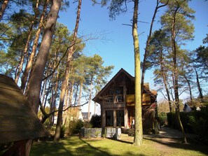 Una cabaña de madera rodeada de altos árboles, con un cielo despejado.
