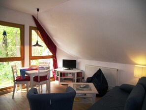 Una habitación acogedora con techo inclinado, una mesa de comedor con sillas, un televisor, una estantería y un sofá.
