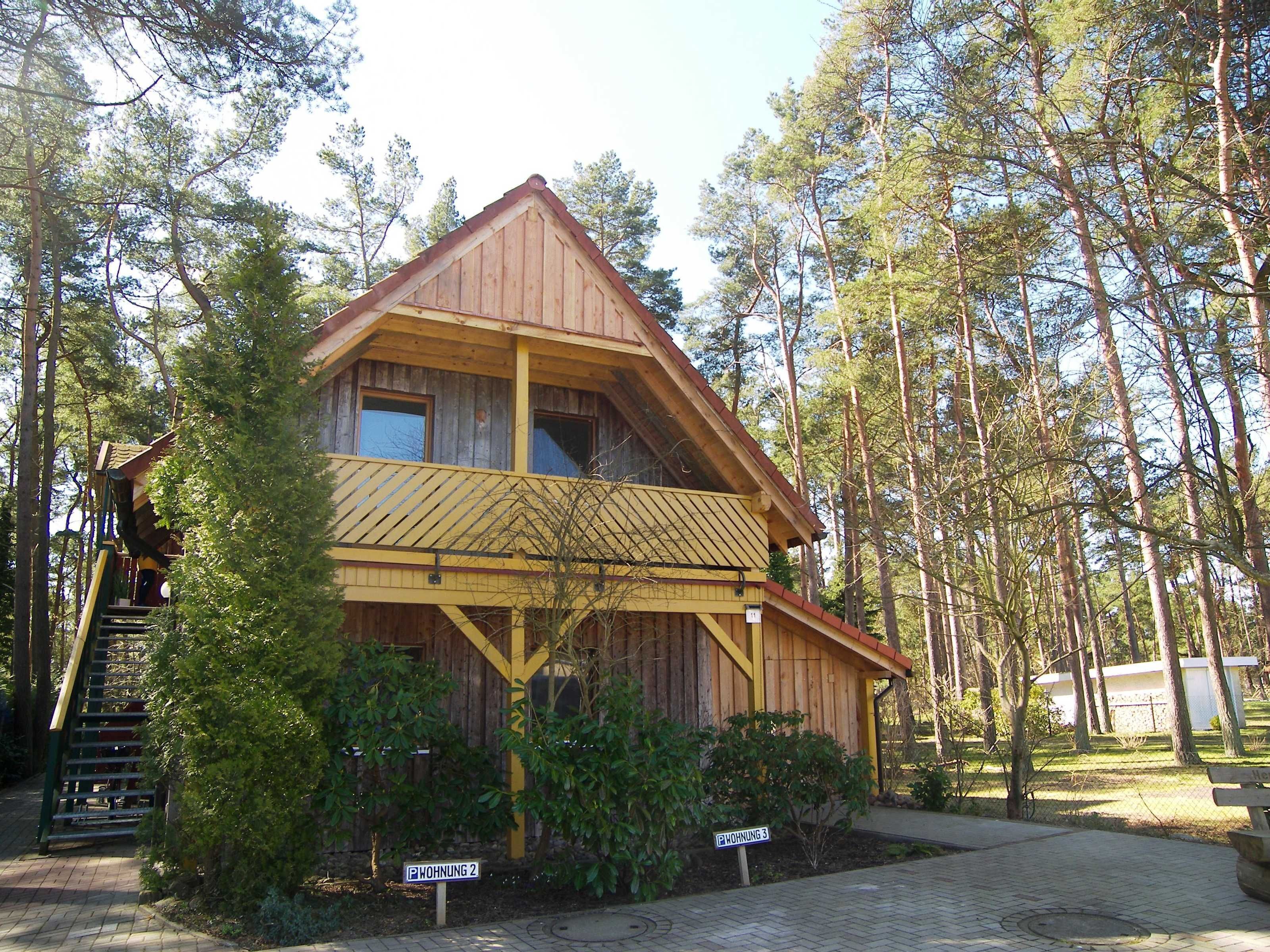 Une cabane en bois dotée d’un balcon, entourée d’arbres.