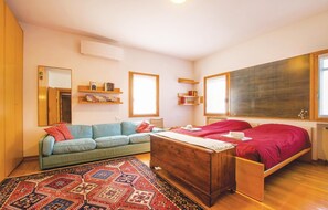 Une pièce comprenant un lit, un canapé, une commode en bois, un tapis à motifs et des étagères remplies de livres et d’objets décoratifs.