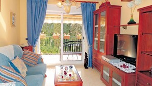 A living room with a sofa, coffee table, TV, and a balcony with blue curtains. - Cozy apartment in Jerez de la Frontera (Jerez de la Frontera)