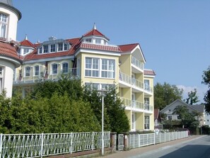 A multi-story building with balconies, a red-tiled roof, and a white fence in front.