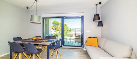 En moderne stue med spiseplads, sofa og et bord med stole. Et stort vindue giver udsigt til det fri.
