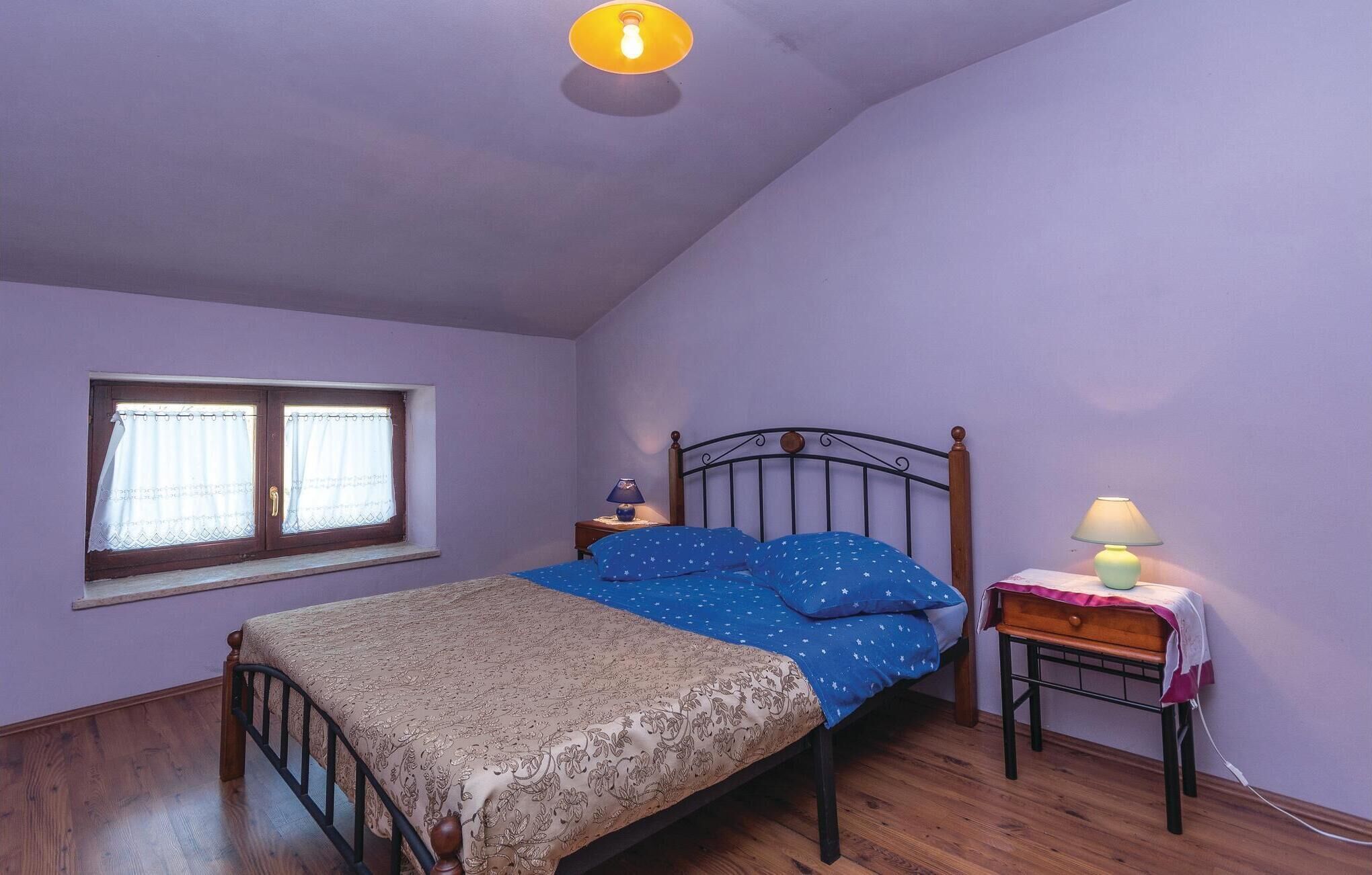 Une chambre à coucher avec un lit, une table de chevet, une fenêtre avec des rideaux et une lampe.