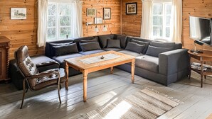 Una sala de estar acogedora con un sofá seccional, una mesa de centro de madera, un sillón de cuero y un televisor sobre un mueble de madera.