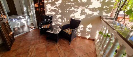 Un espace patio aménagé avec deux fauteuils en osier, une petite table et un tapis décoratif.