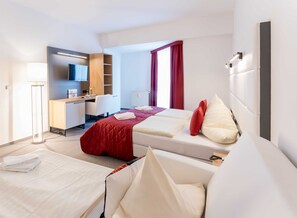 Une chambre d’hôtel avec un lit, un bureau, une chaise, une télévision et une fenêtre avec des rideaux.