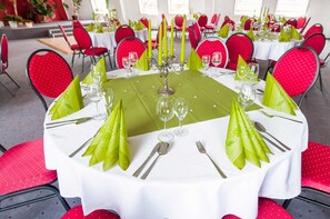 A round dining table with white tablecloth, green napkins, and red chairs. - Triple room - Hotel Stadtfeld (Magdeburg)