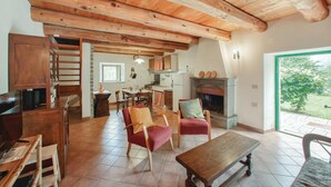 Ein rustikales Interieur mit freiliegenden Holzbalken, einem Essbereich, einem Kamin und Blick ins Grüne.