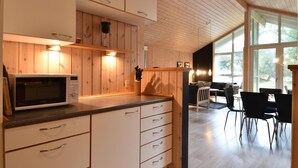 A modern kitchen with wooden cabinetry, a microwave, and a dining area with chairs and a table. - Cozy home in Ringkøbing with kitchen (Ringkøbing)