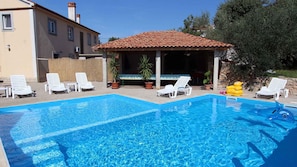 A rectangular swimming pool with clear blue water, surrounded by white lounge chairs and potted plants.