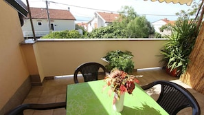 A balcony with a table and chairs, a potted plant, and a view of houses and trees.