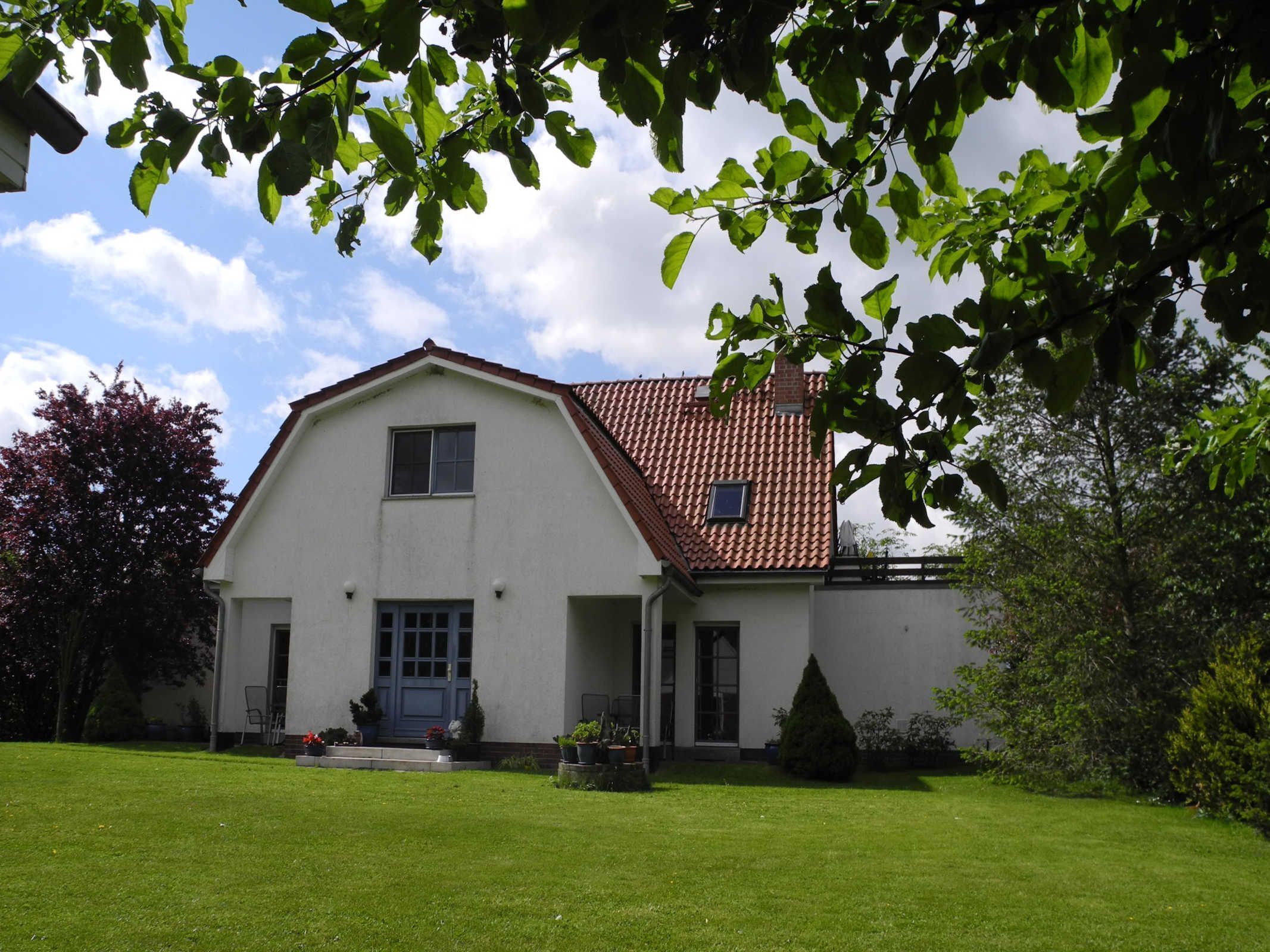 Ein zweistöckiges Haus mit rotem Ziegeldach, einer Veranda und einem gepflegten Rasen.