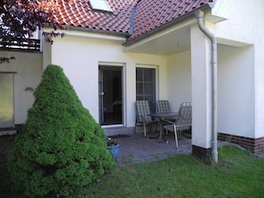 A covered patio with a table and chairs, a potted plant, and a door leading to a room.