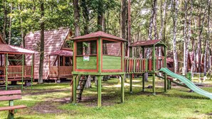 Ein Spielplatz mit Holzspielgeräten, darunter eine Rutsche und Kletterbereiche, umgeben von Bäumen.