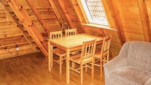 Ein Holzinnenraum mit schrägen Decken, einem Holztisch mit Stühlen und einem Fenster mit einem weißen Rollo.