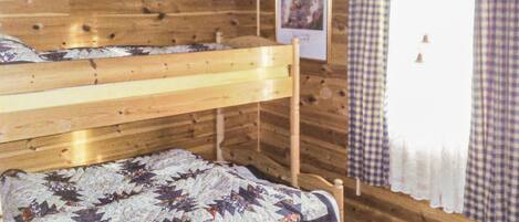 Una habitación de cabaña de madera con literas y una colcha acolchada.